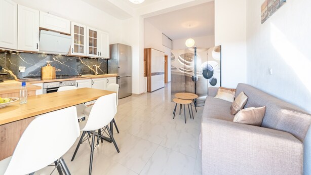 A modern kitchen with white cabinets, a marble backsplash, and a wooden dining table with chairs. - Melissa apartment - stunning sea views, large garden and parking (Korfu)