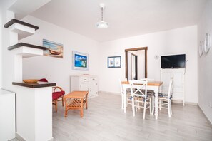 A modern kitchen with white cabinets, a dining area with white chairs, a TV mounted on the wall, and a ceiling fan.