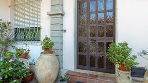 A building entrance with a large potted plant, a metal gate, and a wooden door. - Sartiglia Domu, oasis of relaxation in the heart of Oristano with terrace and Wi-Fi (Oristano)