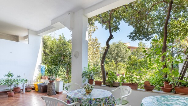 A covered patio with a round table and chairs, surrounded by potted plants and a view of trees. - Sartiglia Domu, oasis of relaxation in the heart of Oristano with terrace and Wi-Fi (Oristano)