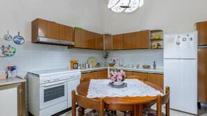 A kitchen with wooden cabinets, a white stove, a dining table with a floral tablecloth, and a ceiling light fixture. - Sartiglia Domu, oasis of relaxation in the heart of Oristano with terrace and Wi-Fi (Oristano)