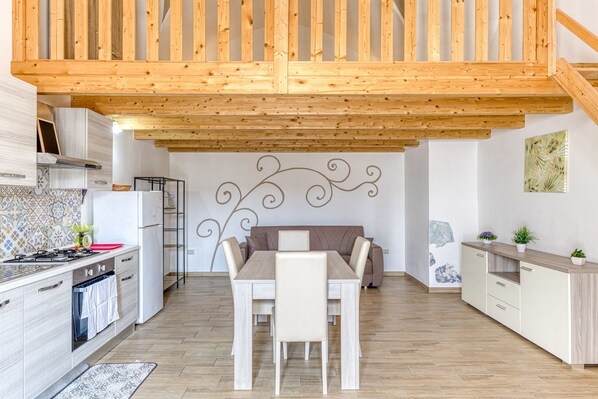 A modern kitchen with wooden beams, a dining table with chairs, a refrigerator, and a stove.