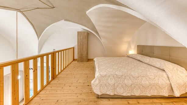 Un dormitorio con piso de madera, una cama con colcha estampada y baranda de madera.