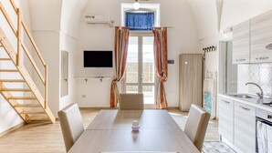Una habitación con una mesa de comedor, sillas, televisor, zona de cocina y una escalera.