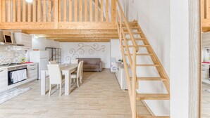Una cocina moderna con comedor, escalera de madera y habitación tipo altillo.