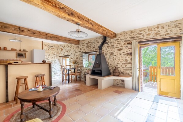 Un intérieur rustique avec des poutres apparentes, un mur en pierre, une cheminée, un coin repas et une porte jaune.