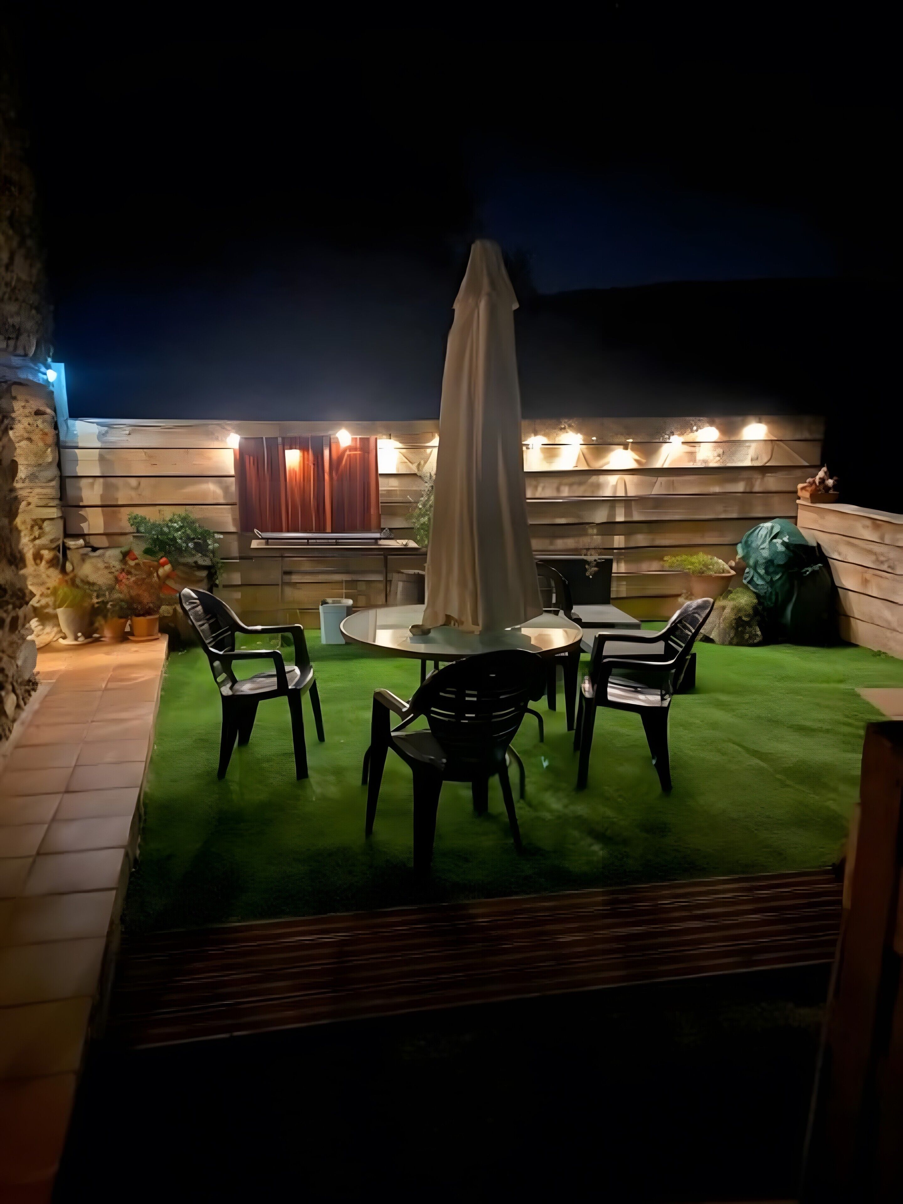 Un patio al aire libre con una mesa redonda, cuatro sillas y una sombrilla.