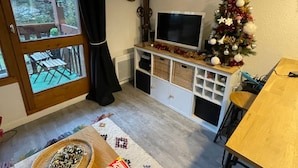 A living room with a TV, a Christmas tree, a wooden table, and a window with a view of trees.