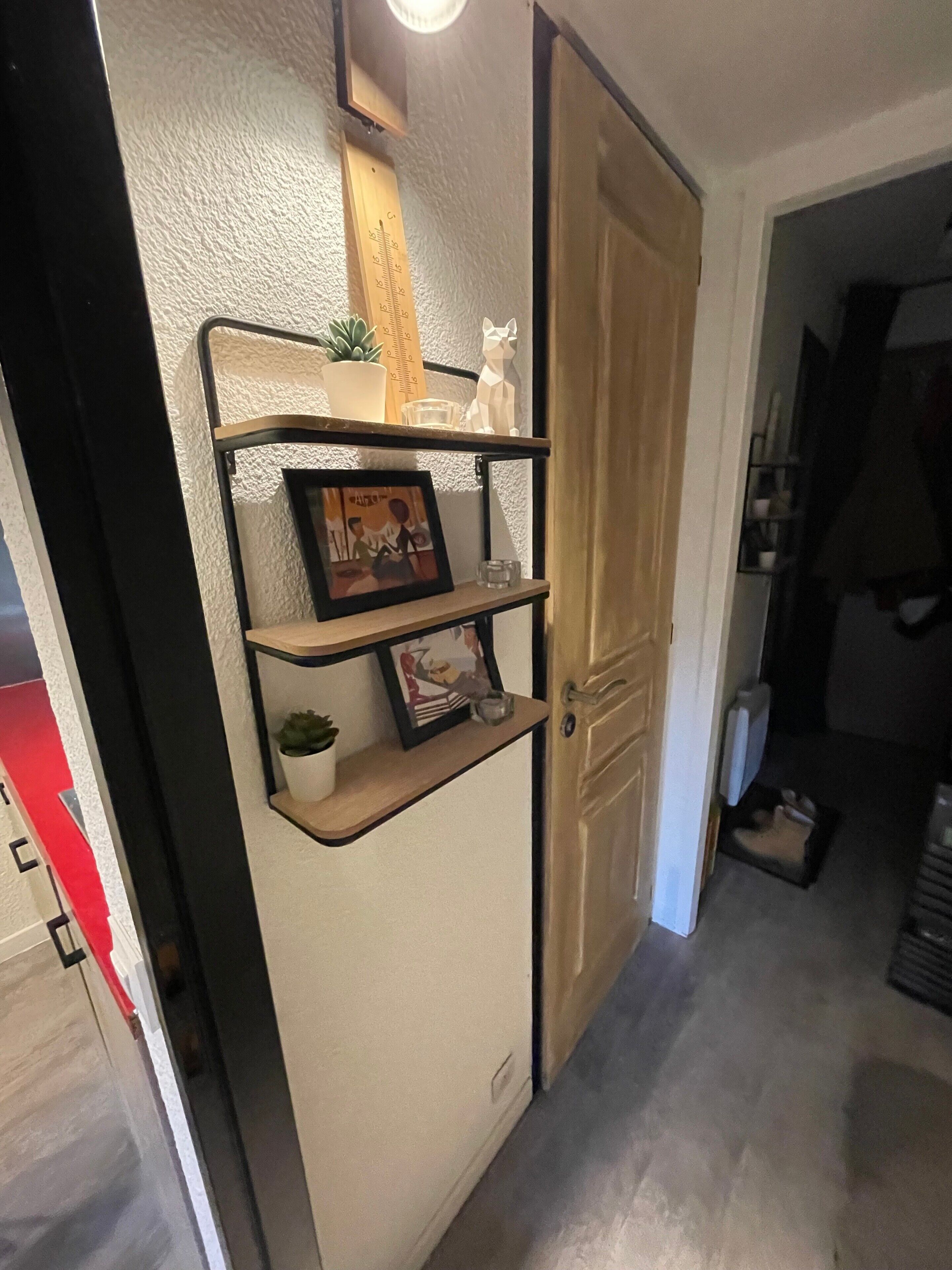 A hallway with a shelf unit containing a plant, a framed picture, and a small figurine.