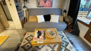 A living room with a grey sofa, a coffee table with books and a decorative bowl, a bookshelf, and a wall mural of a deer.