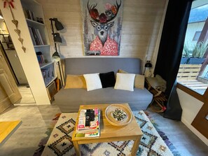 Un salon avec un canapé gris, une table basse sur laquelle sont posés des livres et un vase décoratif, une bibliothèque et une fresque murale représentant un cerf.