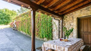 Un área de comedor al aire libre con una mesa preparada para dos personas, una pared de piedra con plantas trepadoras y una estructura de pérgola de madera.