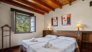 Habitación con dos camas, vigas de madera, ventana con vistas y decoración en las paredes.