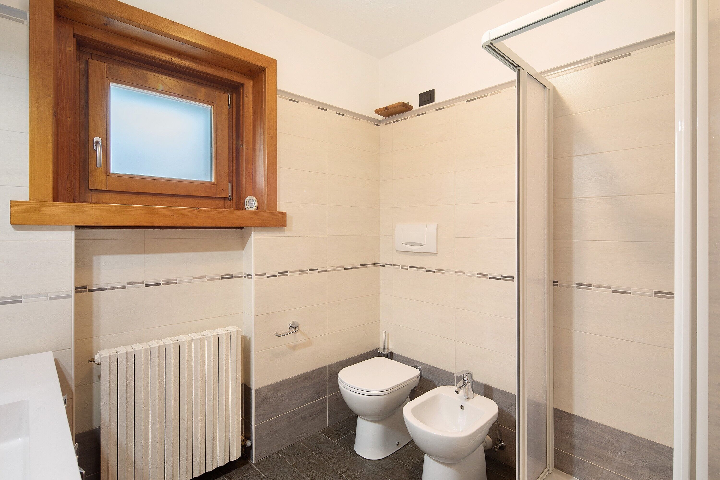 Bany amb dutxa, vàter, bidet i un armari de fusta sobre el vàter.
