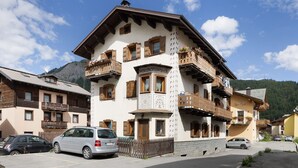 A traditional chalet-style building with multiple balconies, a wooden fence, and a mountainous backdrop.