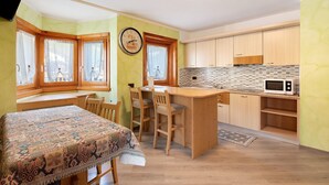 A kitchen with a wooden table, chairs, a microwave, and a clock on the wall.