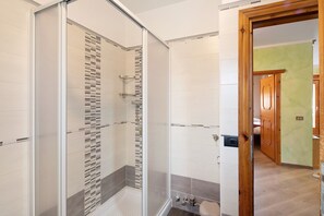 A bathroom with a glass shower enclosure, a toilet, and a sink.