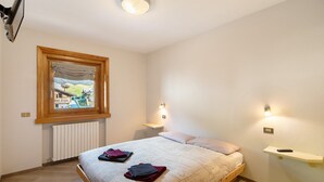 A bedroom with a wooden bed, a window with a view, bedside lamps, and a shelf.