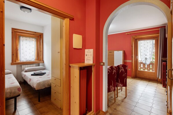 A room with two beds, a wooden wardrobe, a small desk, and a window with curtains.