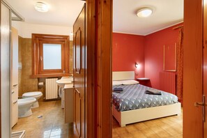 A bedroom with a bed, a nightstand, a wall-mounted TV, and a bathroom with a toilet and sink.