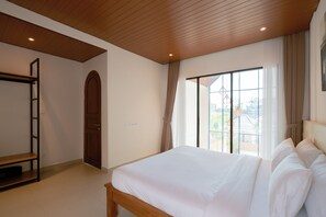 Un dormitorio con techo de madera, un ventanal con cortinas, una cama con ropa de cama blanca y un armario de madera.