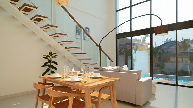 Un interior moderno con una mesa de comedor de madera dispuesta para cuatro personas, un sofá y una escalera con jardineras integradas.