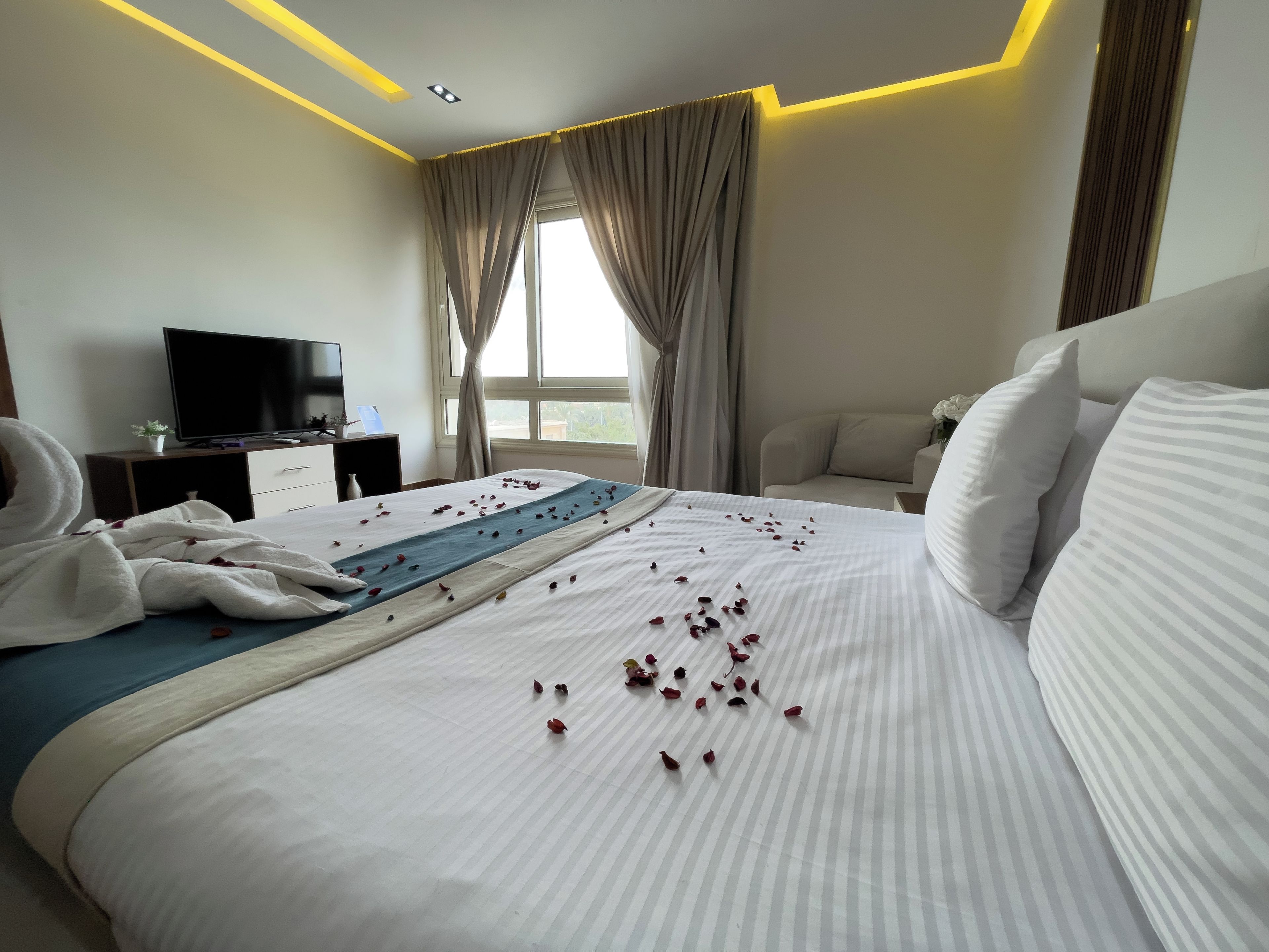 A hotel room with a bed, a television, a desk, and a window with curtains.