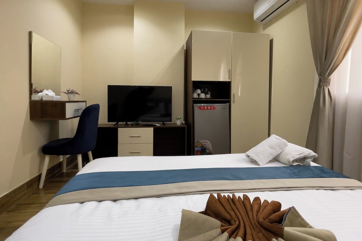 Ein Hotelzimmer mit Bett, Schreibtisch, Stuhl, Fernseher, Kleiderschrank und Klimaanlage.