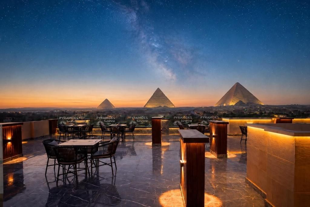 A rooftop terrace with tables and chairs, a bar area, and the pyramids in the background.