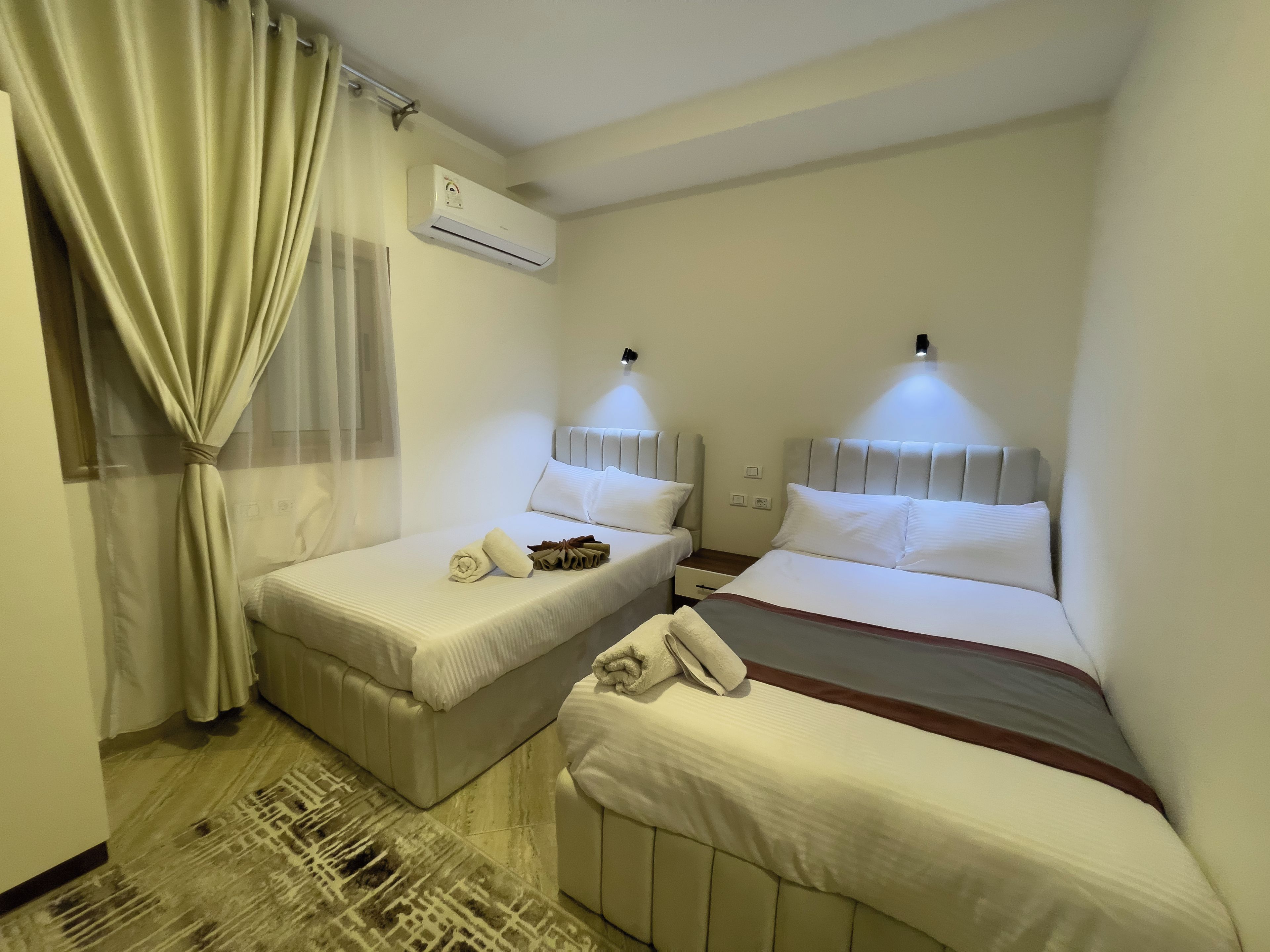 A hotel room with two beds, a curtain, an air conditioning unit, and a patterned rug.
