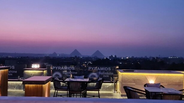 A rooftop bar with "PYRAMIDS Sunshine Inn" signage, outdoor seating, and a view of the pyramids in the background.
