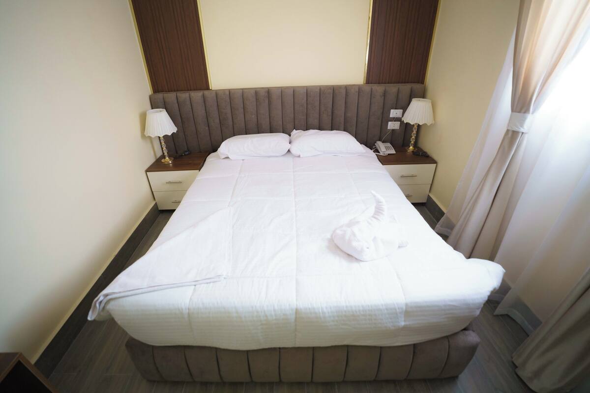 A neatly made bed with white linens, two bedside lamps, a phone on the nightstand, and a wooden headboard.