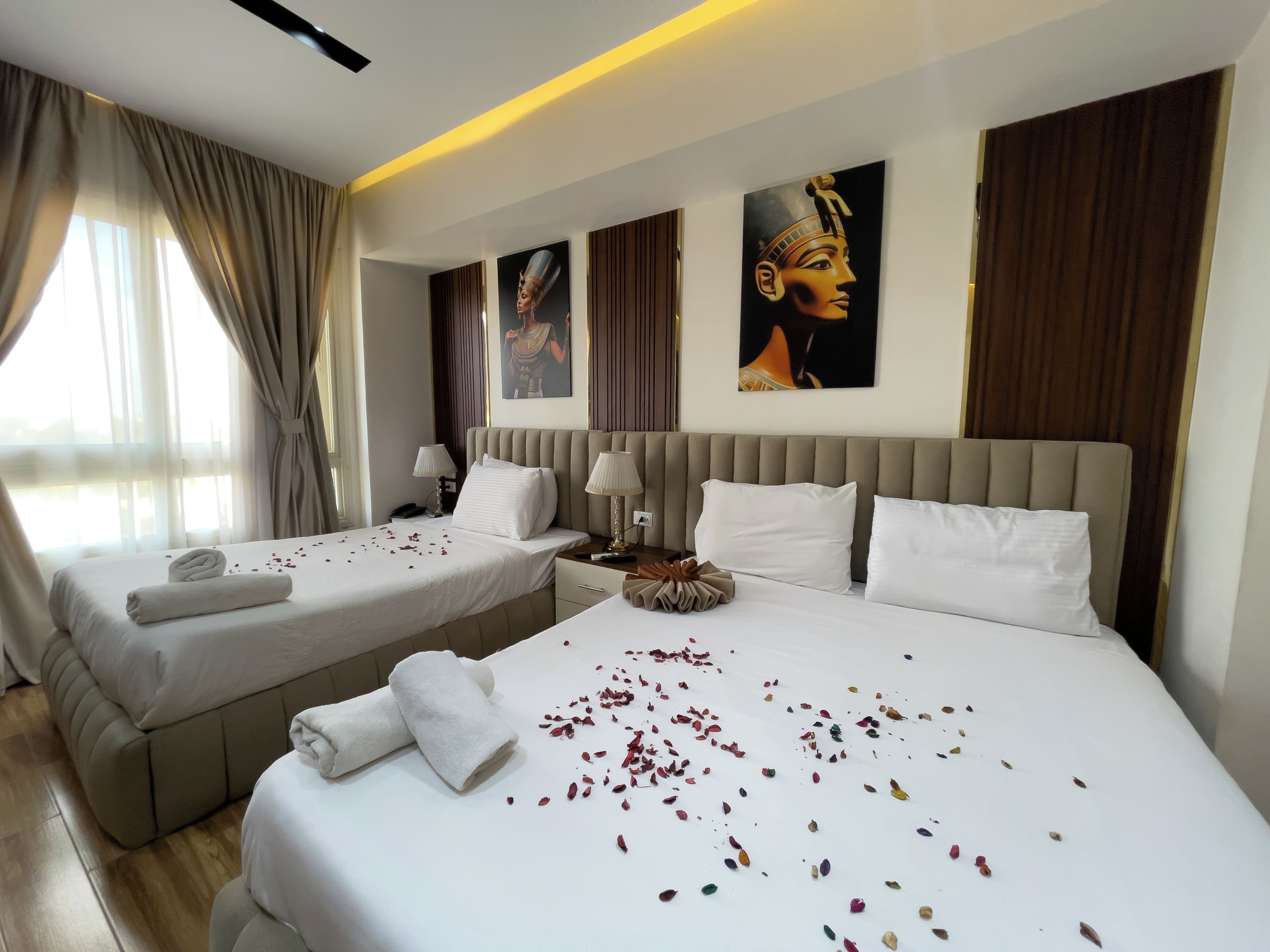 A hotel room with two beds, a large window with curtains, and artwork on the walls.