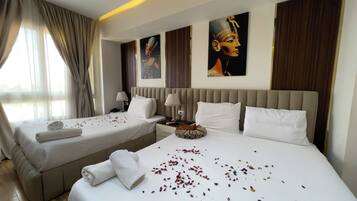 A hotel room with two beds, a large window with curtains, and artwork on the walls.
