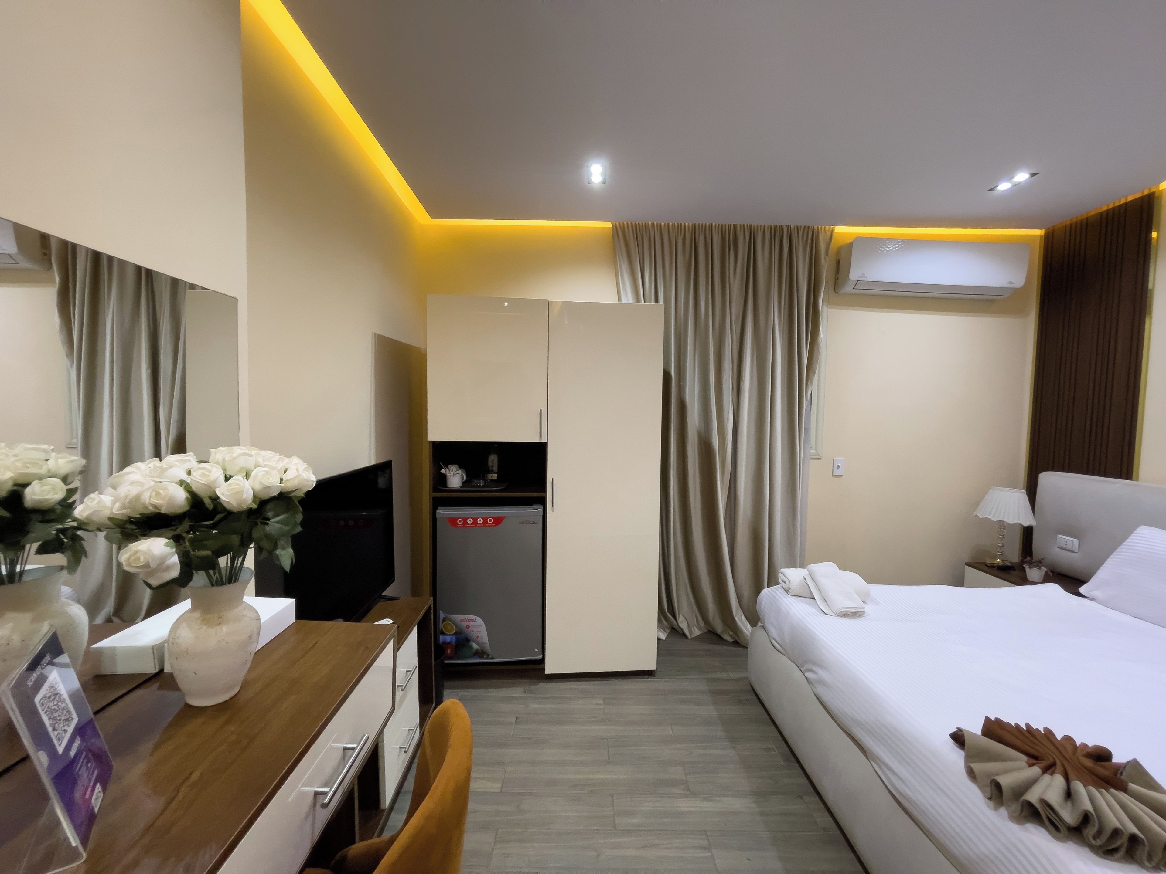 Habitación de hotel con cama, escritorio con computadora, refrigerador y armario.