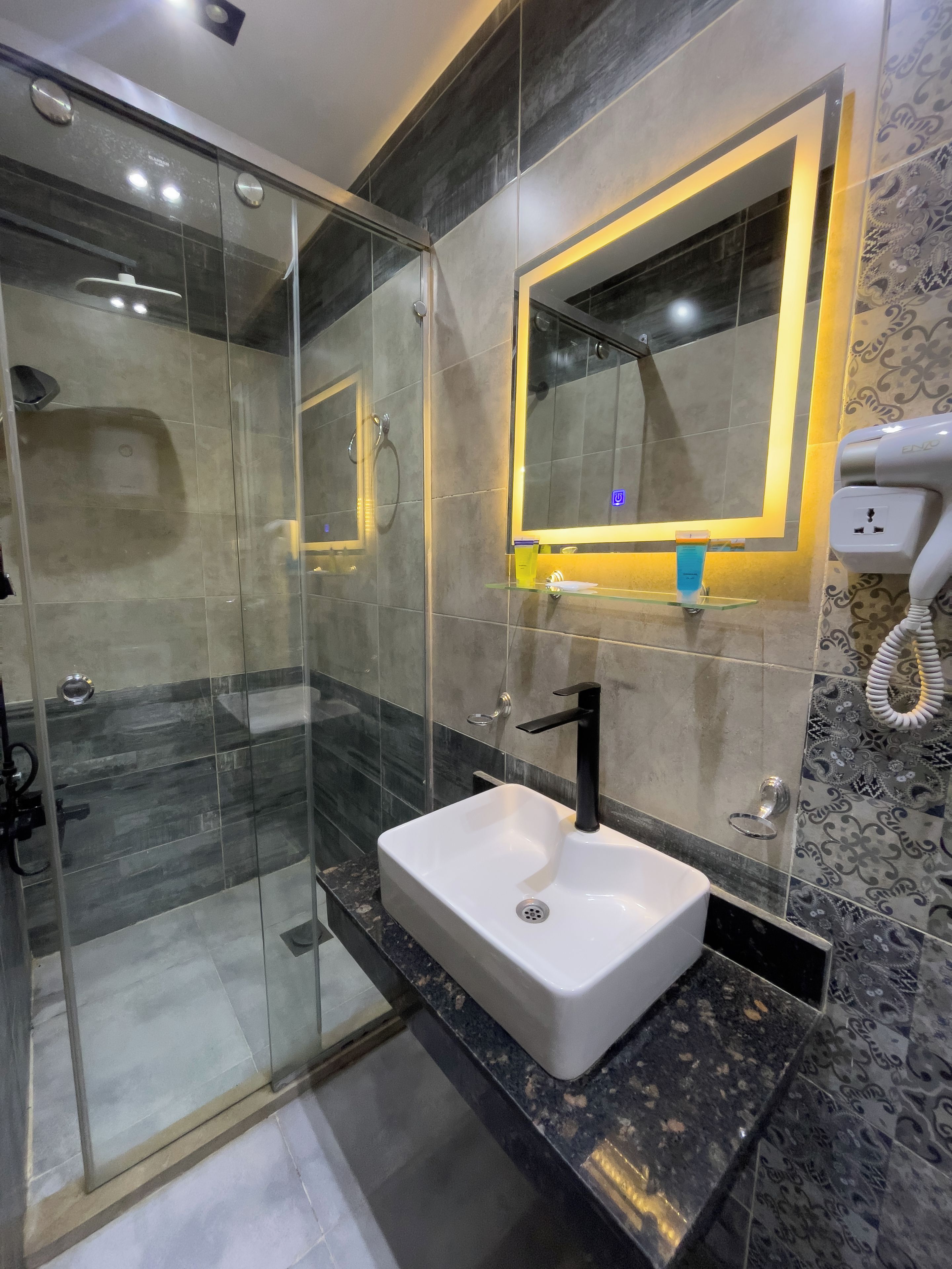 A modern bathroom with a glass-enclosed shower, a white sink with a black faucet, and a mirror with a decorative frame.
