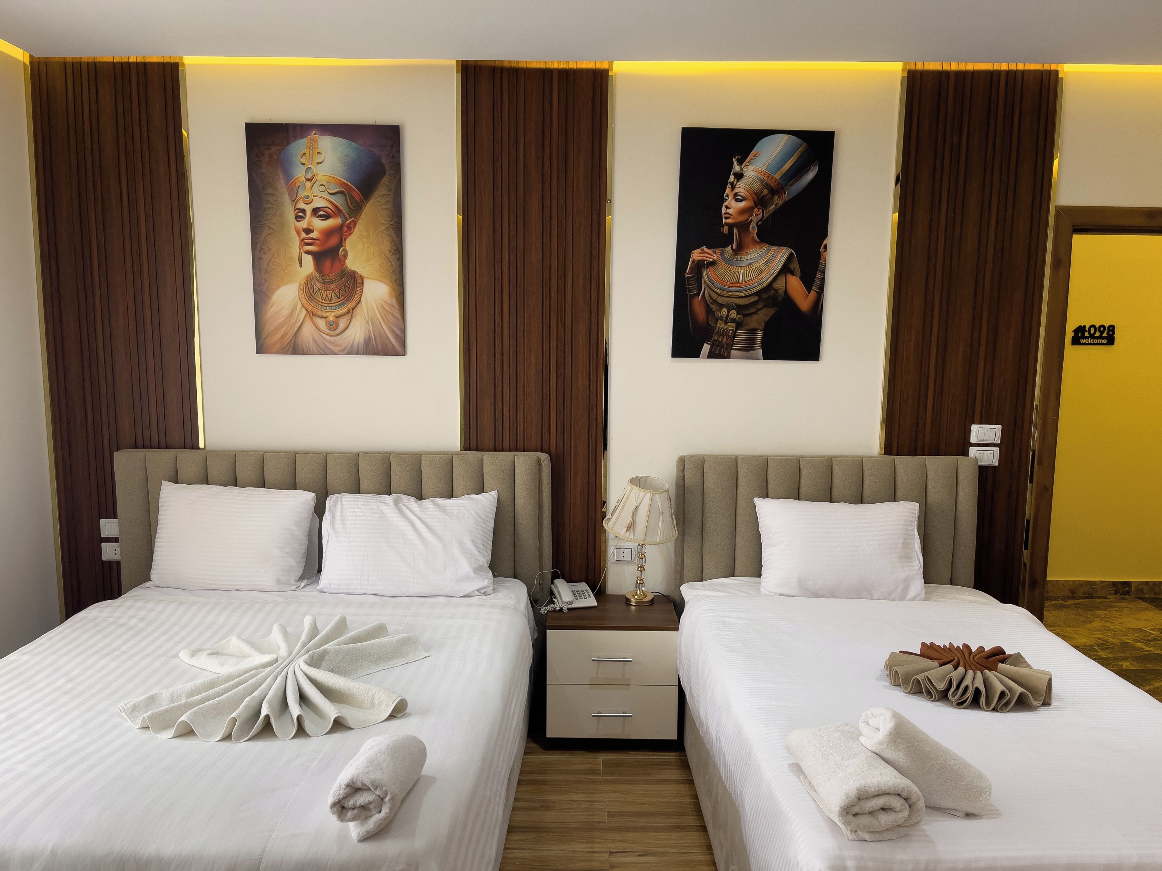 A hotel room with two beds, a nightstand, and artwork on the walls.