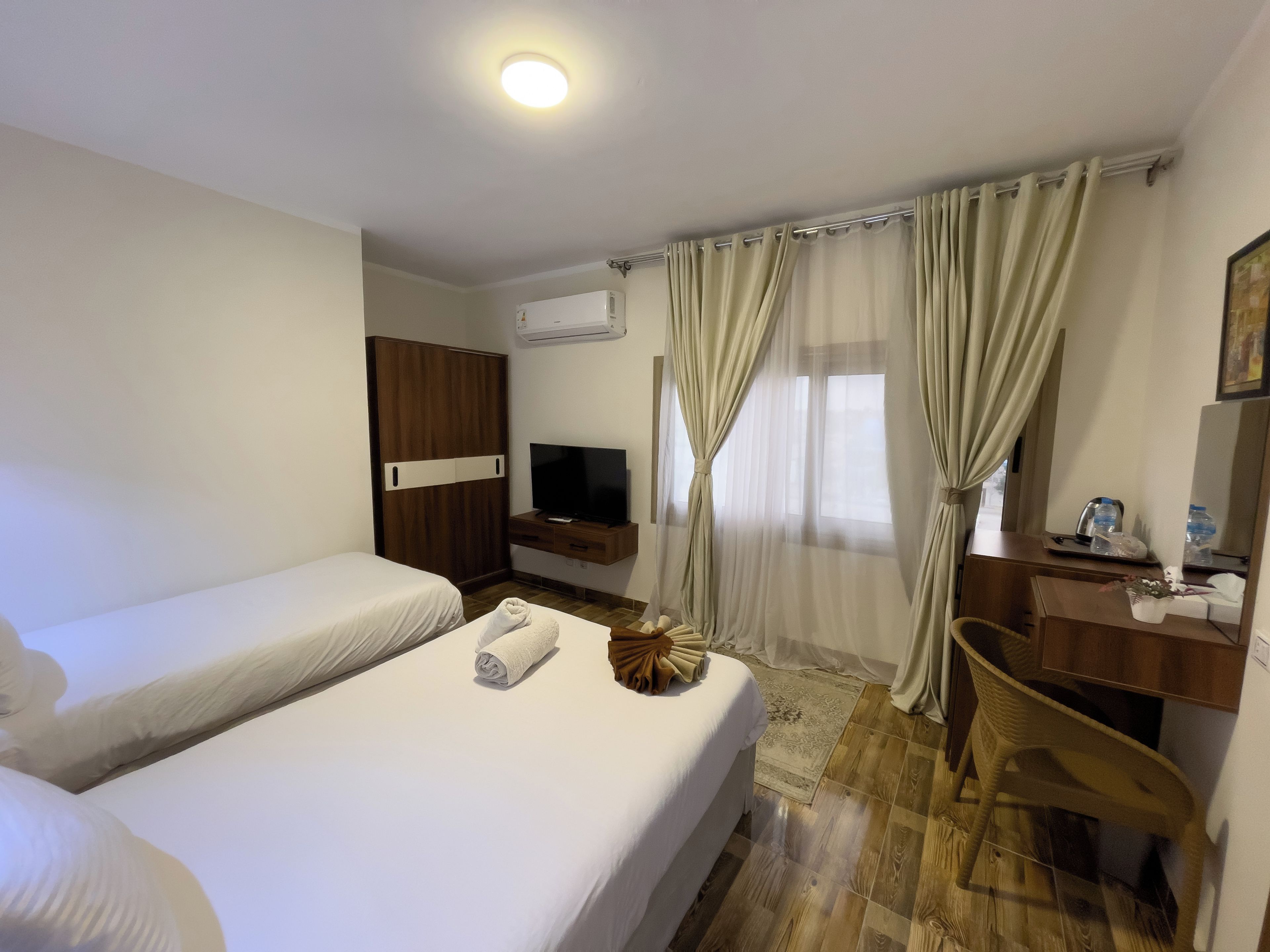 Quarto de hotel com duas camas, televisão, escrivaninha e janela com cortinas.