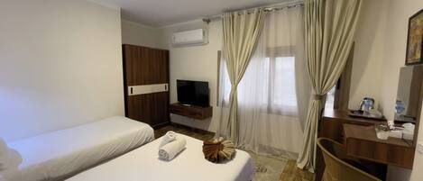 Quarto de hotel com duas camas, televisão, escrivaninha e janela com cortinas.