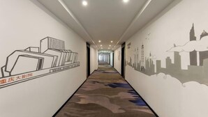 Un couloir doté d’un tapis à motifs, de murs ornés de fresques représentant des paysages urbains et d’un éclairage encastré.