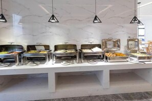 A buffet with multiple food stations, each with a glass container and a metal tray, set against a marble wall with pendant lighting. - Fengyelin Hotel (Chongqing)