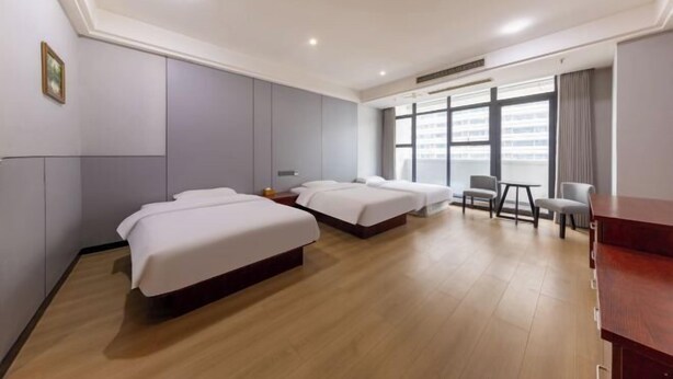 Une chambre d’hôtel avec trois lits, un plancher en bois, un bureau et une fenêtre donnant sur la ville.