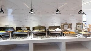 Un buffet proposant une variété de plats, notamment des fruits, des légumes et des viandes, disposés sur un comptoir en marbre, le tout éclairé par des lampes suspendues.