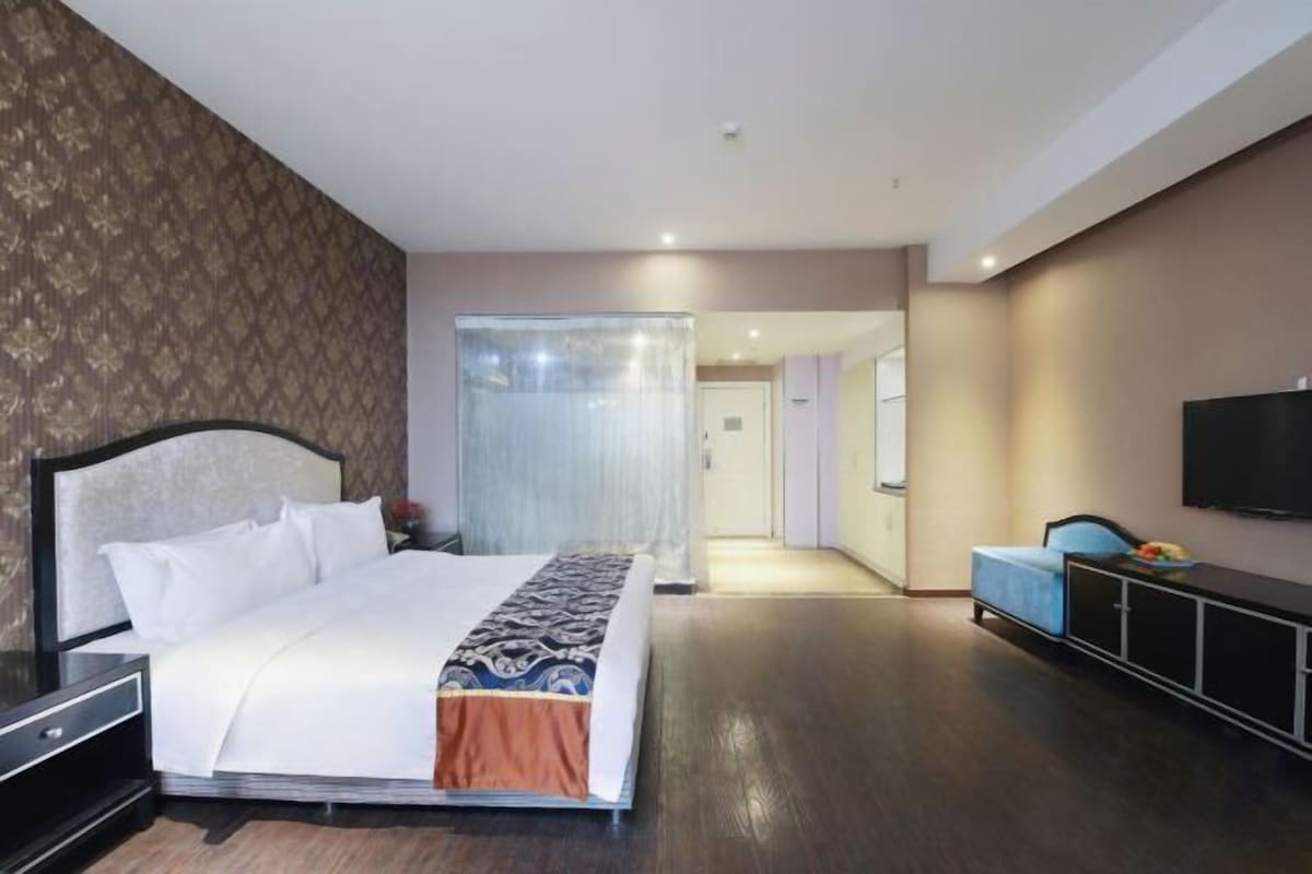 Ein modernes Hotelzimmer mit einem großen Bett, einem an der Wand montierten Fernseher und einer separaten Sitzecke mit einem blauen Sofa.