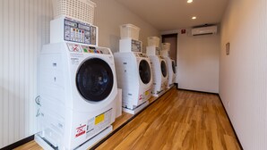 A row of front-loading washing machines in a hallway with wooden flooring and white walls. - HOTEL R9 The Yard Yamanashichuo (Chuo)