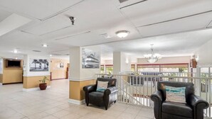 Eine geräumige Lobby mit hoher Decke, einem Empfangstresen, zwei Ledersesseln und einer Treppe, die zu einer oberen Ebene führt.
