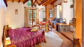 Una habitación acogedora con cama, una mesa de madera y un sofá. Hay ventanas y una chimenea de piedra.