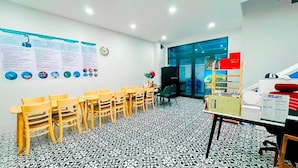 A conference room with a patterned floor, wooden chairs, a table with a vase of flowers, and a wall with informational posters. - The Beach Homestay (Phu Quoc)