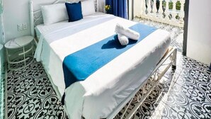 A hotel room with a bed, a small bedside table, a window with a view of buildings, and patterned floor tiles. - The Beach Homestay (Phu Quoc)