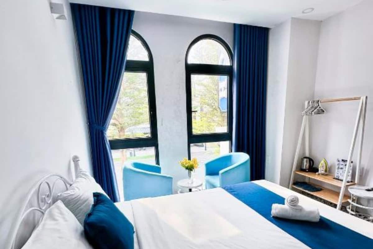 A hotel room with a bed, a small table with a vase of flowers, and a chair.